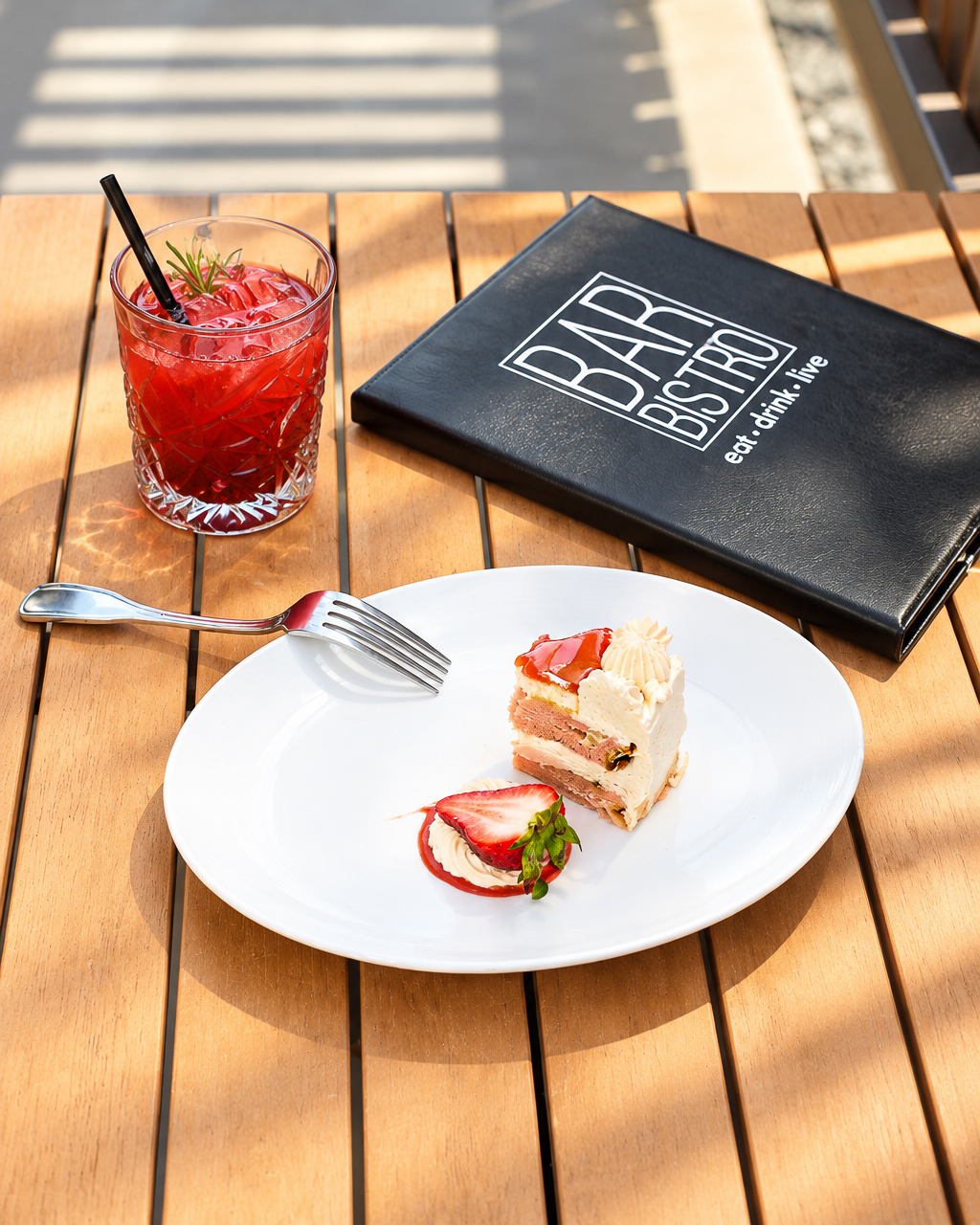 Sunlight service: cake, a cocktail and the menu on a sunny patio table at Bar Bistro