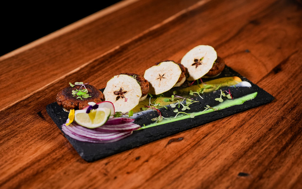 A plated starter on slate with apple crisps and greens, on a wood table at Chutneys